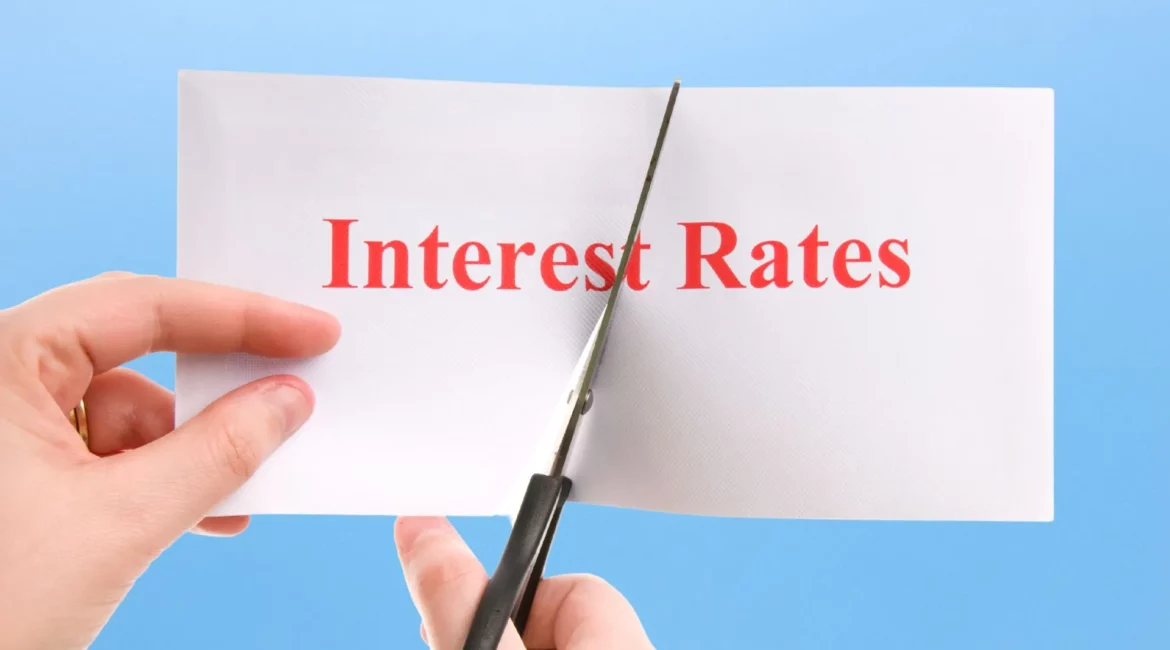 A hand cutting interest rates on a piece of paper with a pair of scissors.